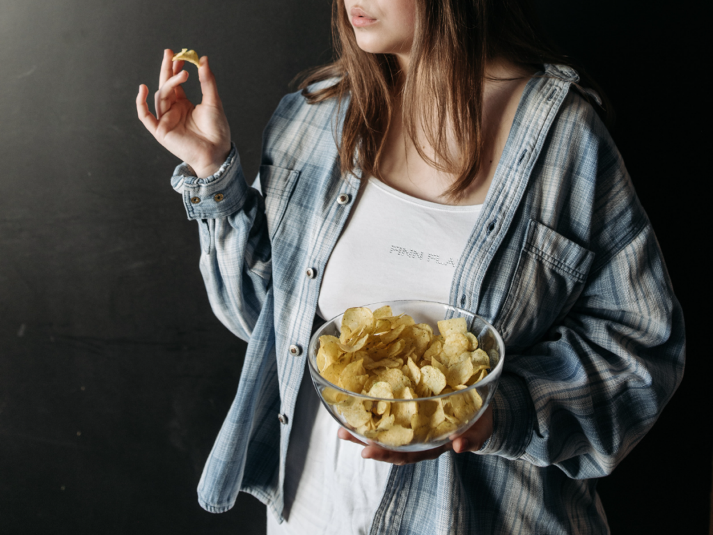 Person eating mindfully with chips in a bowl to learn how to stop overeating at night.