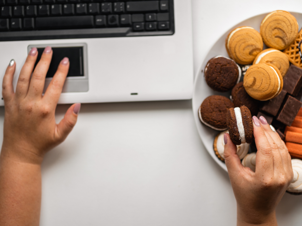 Hands typing on a laptop and grabbing snacks at same time - signs of comfort eating