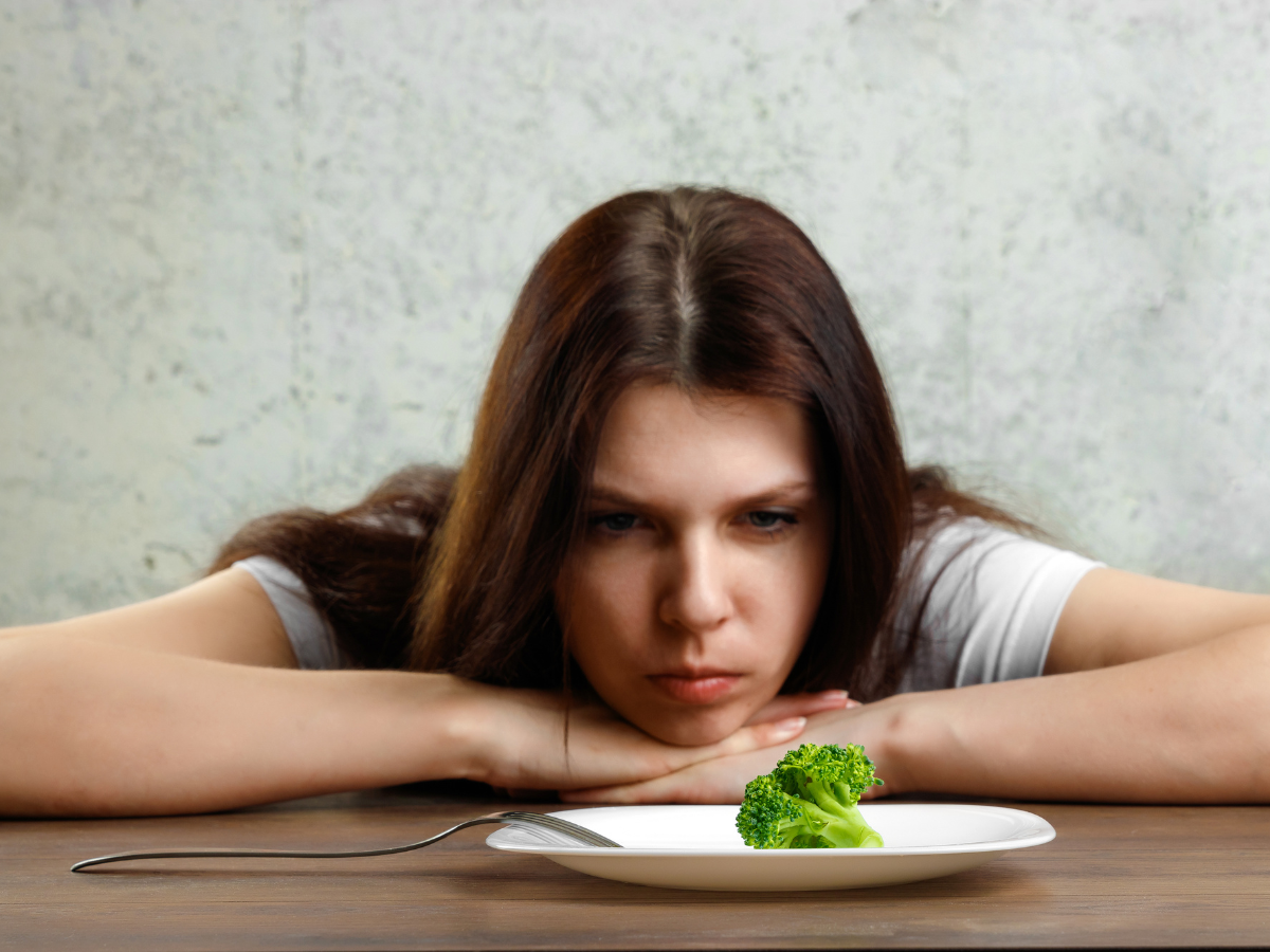 Women staring at broccoli on a plate looking frustrated. Food is not the enemy!