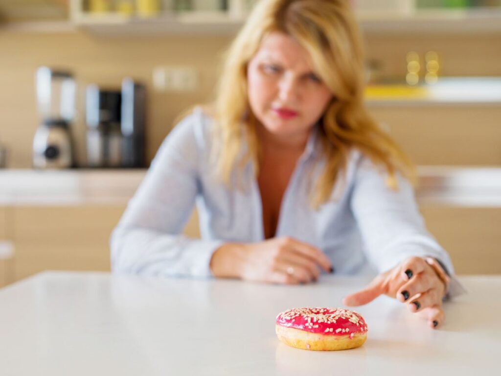 woman reaching for a donut thinking about weight gain and sugar cravings