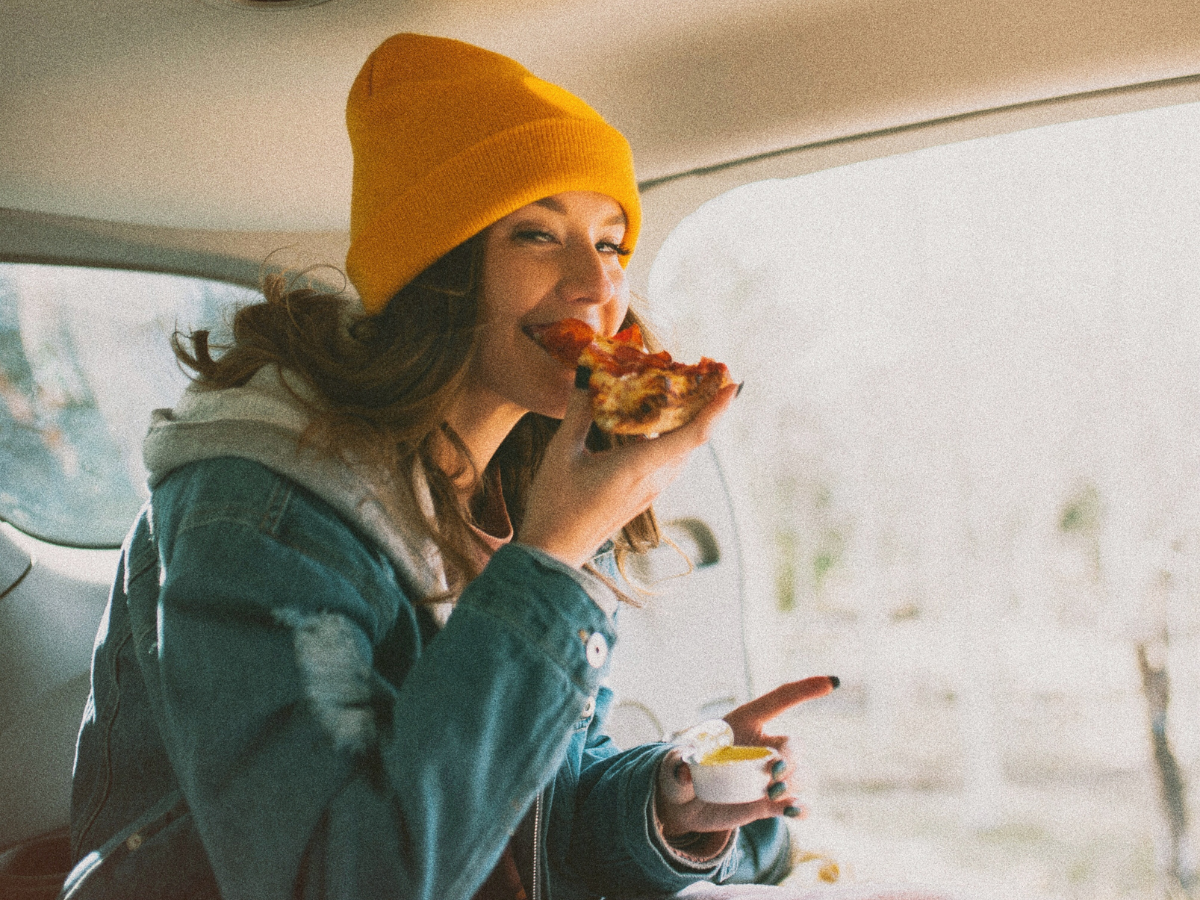 Girl wearing an orange hat and eating a piece of pizza learning about cannabis and intuitive eating to prevent the binge eating munchies