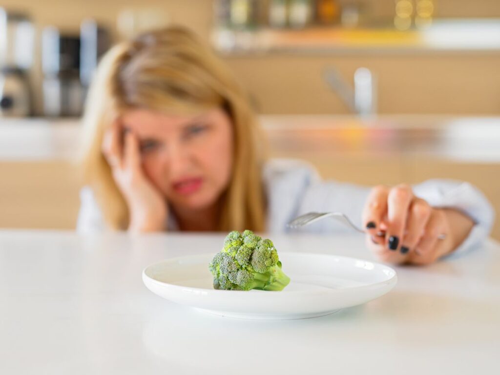New year diet temptation with lady poking at a piece of broccoli on a plate looking frustrated