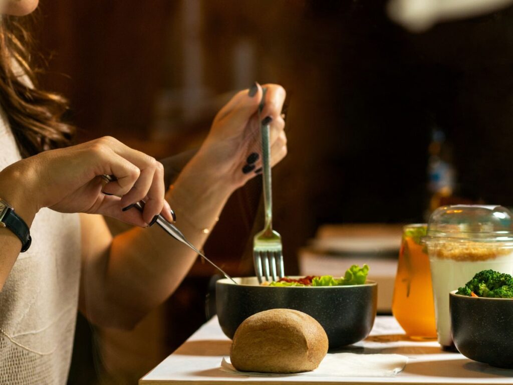 Woman's hands holding forks while eating out of a bowl and craving veggies