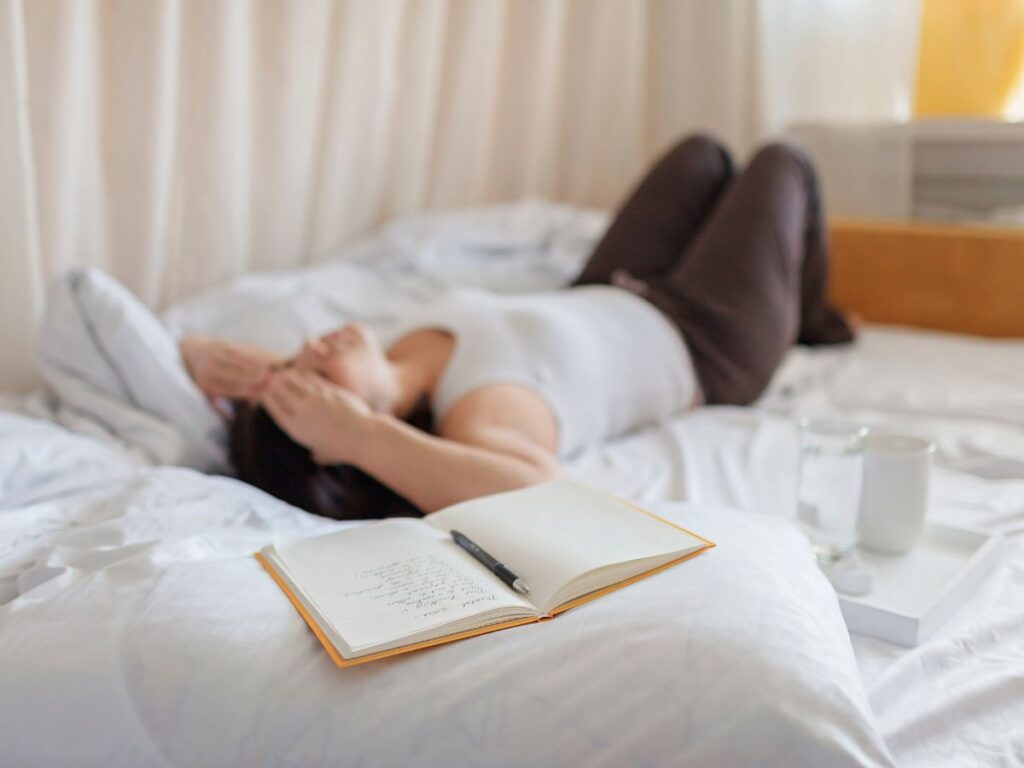 woman laying on a bed looking frustrated with a notebook in front of her having mindset struggles with intuitive eating